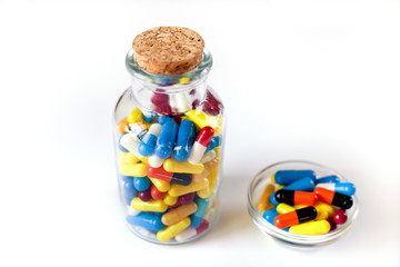 Colorful medicine capsules in a transparent bottle, and in a small bowl near, on a white background, isolate