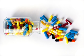 heap of multi-colored medical capsules in a transparent bottle on a white background, scattered from a bottle. top view, isolate