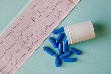 blue capsules spilling out of a bottle on a blue background near the cardiogram.