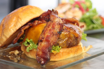 Burger on a Bun with Bacon Sitting  on a Glass Plate