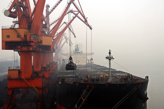 Cargo terminal for discharging coal cargos by shore cranes during foggy weather. Port Bayuquan,China. January, 2020.