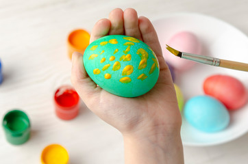 Child is painting egg in different color for Easter holiday, face is not visible