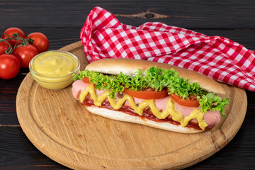 Hot dog with mustard, tomato and lettuce on wooden background