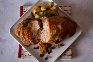 Roast turkey leg with potatoes, cranberries and rosemary on white plate. Flat lay, overhead horizontal image