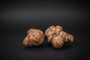 Jerusalem artichoke on a dark background. The concept of eating and using unusual plants for food.