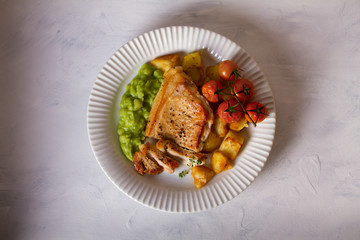 Roast pork chop with mushy peas, potatoes and tomatoes on white plate. View from above, top view