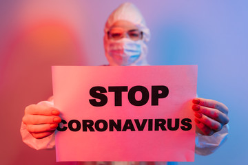 Coronavirus and quarantine concept. Professional doctor in protective suit, glasses and face mask holding hands in front, standing isolated on blue background