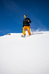Fototapeta na wymiar Winter sports - young man running with snowshoes downhill in high mountains covered with lots of snow