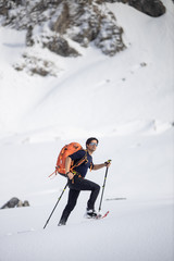 Winter sports - young man walking with snowshoes in high mountains covered with lots of snow (selective focus on the mountain in the background)