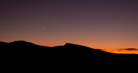 Obraz premium Crescent moon and sunset over silhouette of desert ridge on fall evening