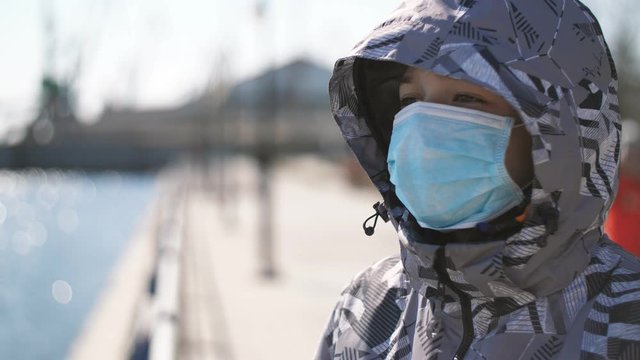 Smart boy in a protective mask and hood standing on a river quay in spring