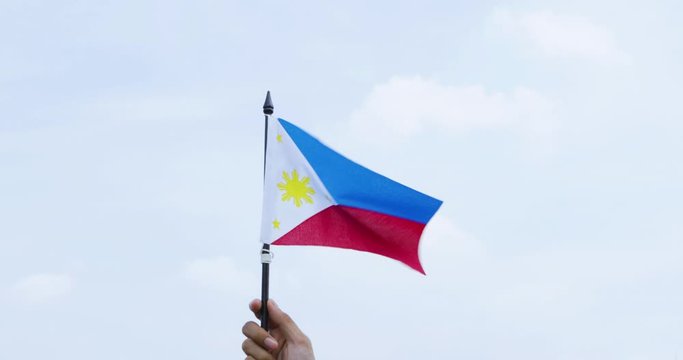 Unknown hand holds Philippine flag under clear sky