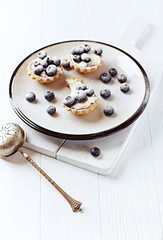 Little mascarpone tart with fresh bilberries on bright wooden background. 