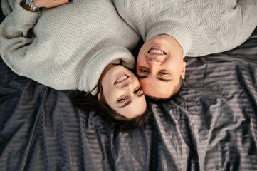 A smiling happy couple is lying on the bed in their bedroom. They have rest together at home. Top view