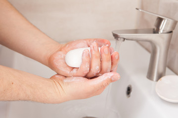 A man holds soap in his hands over the washbasin.