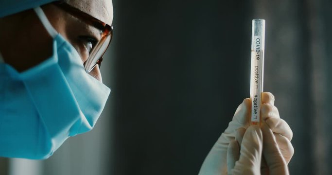 Conceptual 4K video of a doctor holding and looking at a test tube while testing samples for presence of coronavirus (COVID-19).