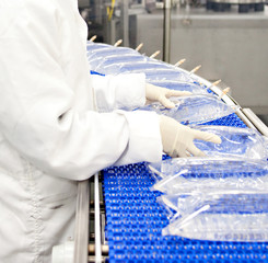 Medical personnel and lab workers wearing gloves work at a conveyor belt producing IV bags for medical care. 