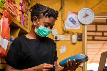 young african female attendant using the point of sale machine to pay for the goods her customer...