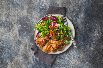 Roasted bbq wings with green salad with tomatoes. Top view