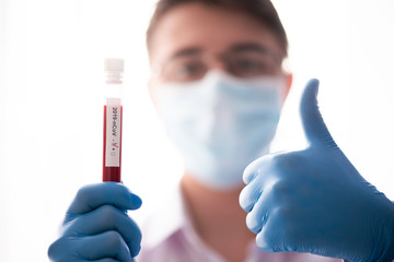Test tube in male hand close up, doctor in medical mask holding vial with red liquid. Concept blood...