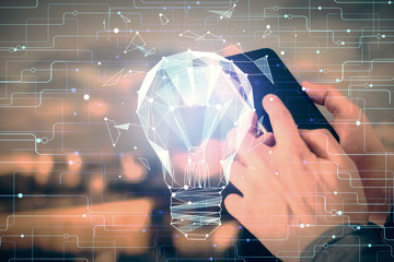 Double exposure of man's hands holding and using a digital device and bulb hologram drawing. Idea concept.