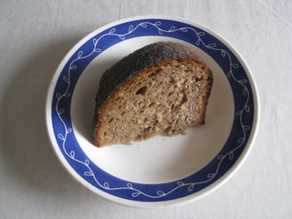 Plato blanco con decoración azul en borde con pedazo de pan de centeno con semillas sobre mantel blanco