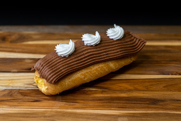 cream filled eclair with chocolate and white icing on a wood board