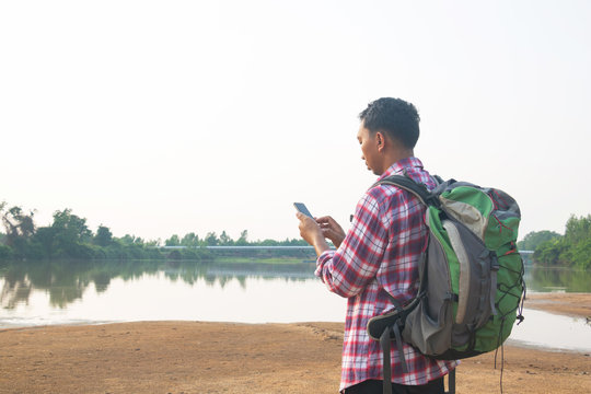 A backpack man standing on the river and see over view in nature.Tourist use smart phone and enjoying fresh air. Thailand.holiday, vacation , Photo Travel and relax time concept.