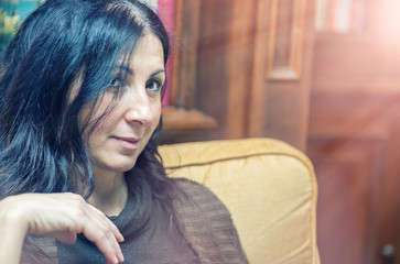 Beautiful brunette woman seated on a chair at home smiling and looking to someone