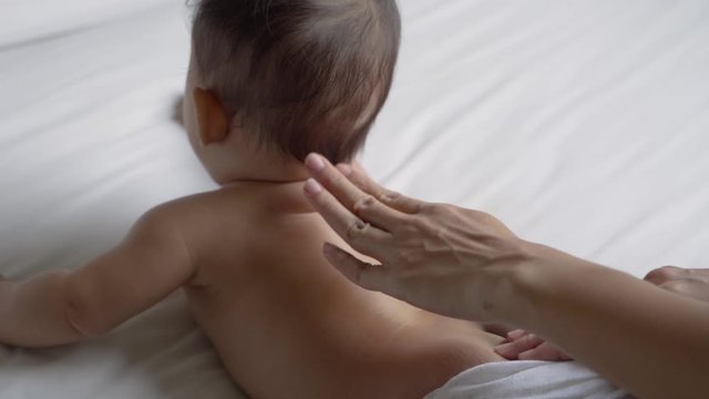prone baby is oiled on his back by his mother while lying in the bedroom