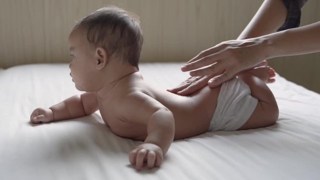 prone baby happy is smile his back by his mother while lying in the bedroom