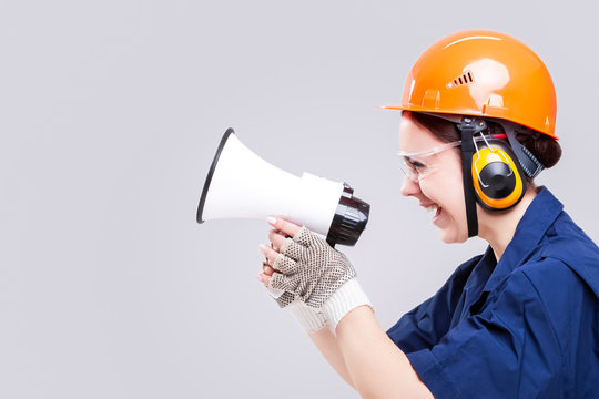 Portrait of Caucasian Female Builder in Protective Kask and Glasses. Posing with Megaphone and Yelling
