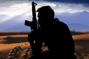 Silhouette of a male soldier resting in the shade on a desert and holding a rifle.  Depicts the...