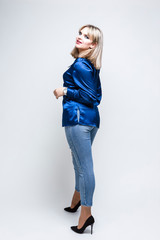 Stylish Alluring Caucasian Blond Girl Posing in Blue Against White. Standing Half Turned