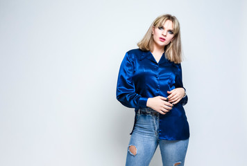 Stylish Alluring Caucasian Blond Girl Posing in Blue Against White. Standing Half Turned.