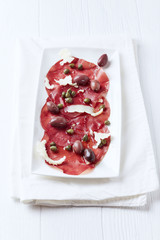 Carpaccio with Kalamata Olives, Capers and Parmesan. Bright wooden background.