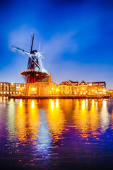 Fototapeta na wymiar Travel Destinations. Night View of Harlem Sight With De Adriaan Windmill on Spaarne River On The Background During Blue Hour.