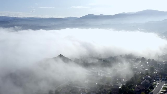 Aerial view, morning mist fog over Los Angeles neighborhood, over clouds showing mountains in the distance