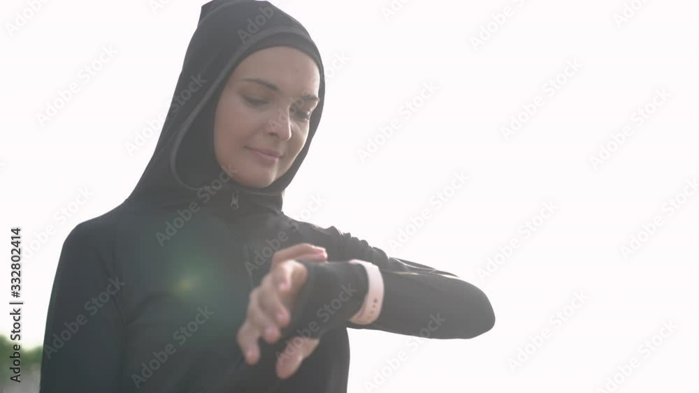 Wall mural young muslim woman with scarf setting smart watch before jogging