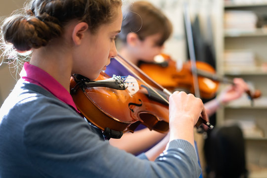 Teenage girls playing violins in classroom