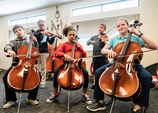 Teenage girls and boys playing cellos and violins in classroom