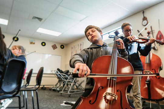 Teenage girl and boy playing cello and violin in classroom - Powered by Adobe