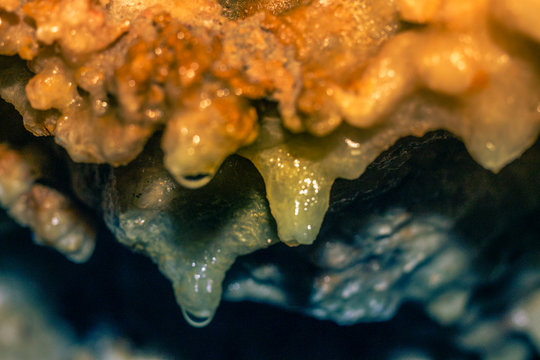 gotas de agua colgando de formaciones minerales en una gruta con colores desde el azul aqua al anaranjado