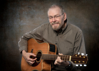Mature man with full beard and thinning gray hair playing six string acoustic guitar texture...