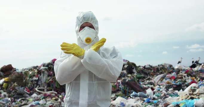 Virologist shows no-sign with crossed hands and nods head near landfill dump