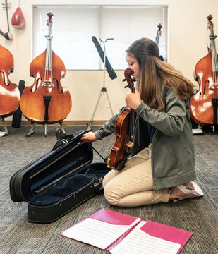 Teenage girl with violin and sheet music kneeling in classroom