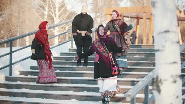 Russian folklore - cheerful women and men are dancing russian dance in the park on the stairs