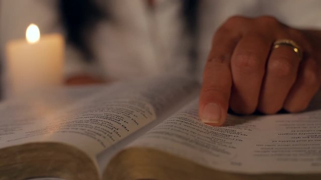 A woman is sitting reading a bible verse with a candle light at night