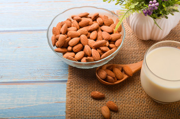 Close up view of healthy almond milk in drinking glass with seed in bowl on wooden background.