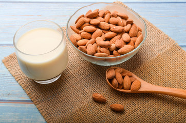 Close up view of healthy almond milk in drinking glass with seed in bowl on wooden background.